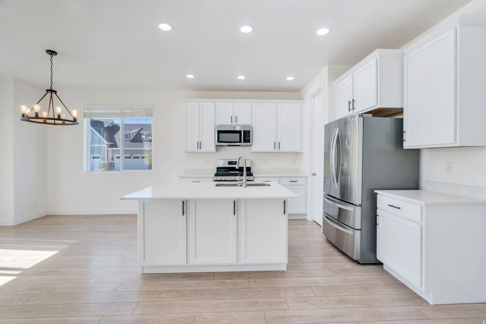 Spacious kitchen featuring an island with a sink, stainless steel appliances, white cabinetry, recessed lighting, and wood-finish flooring