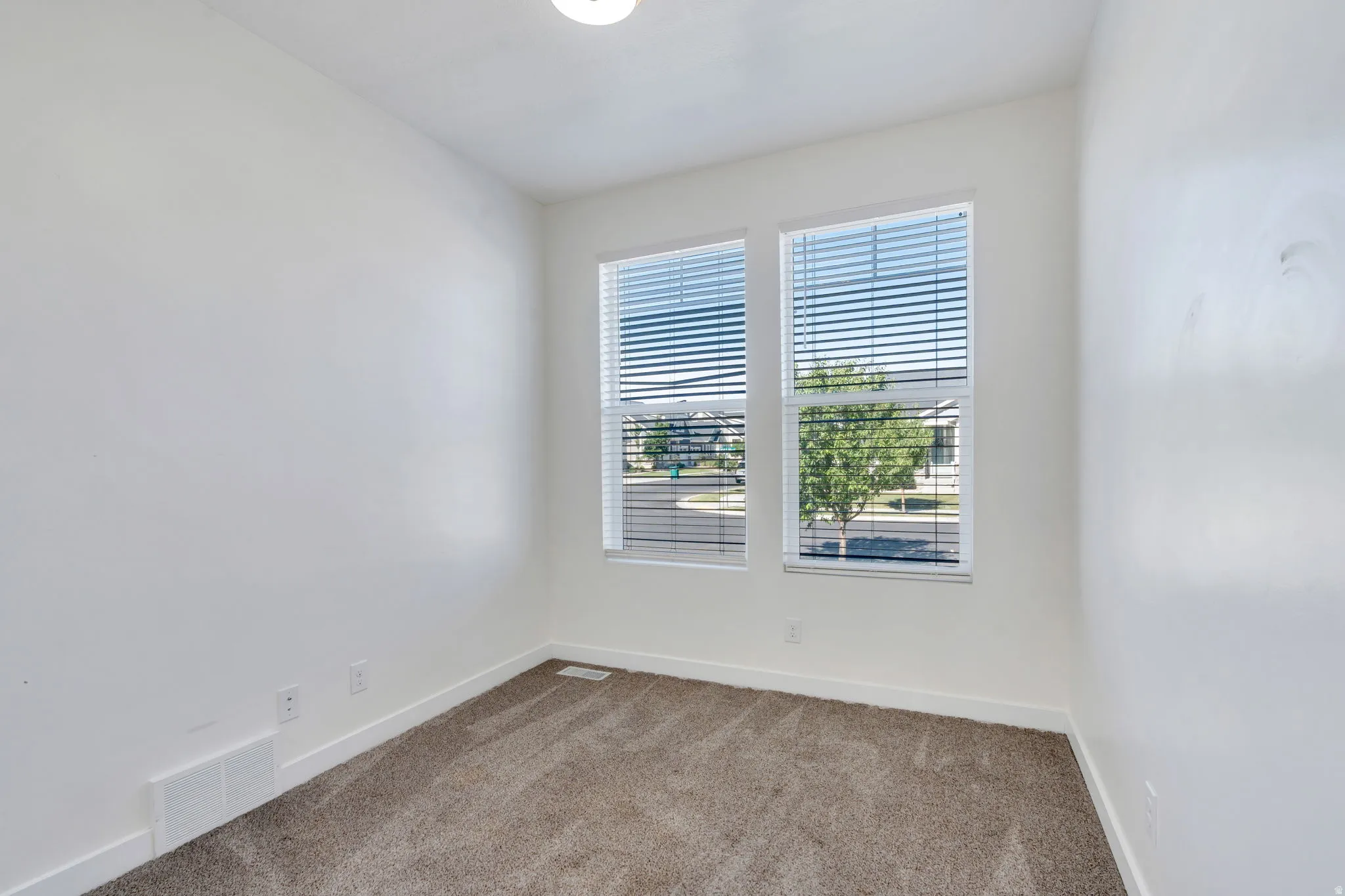 Bright room featuring two windows with horizontal blinds, neutral wall paint, and plush carpet flooring