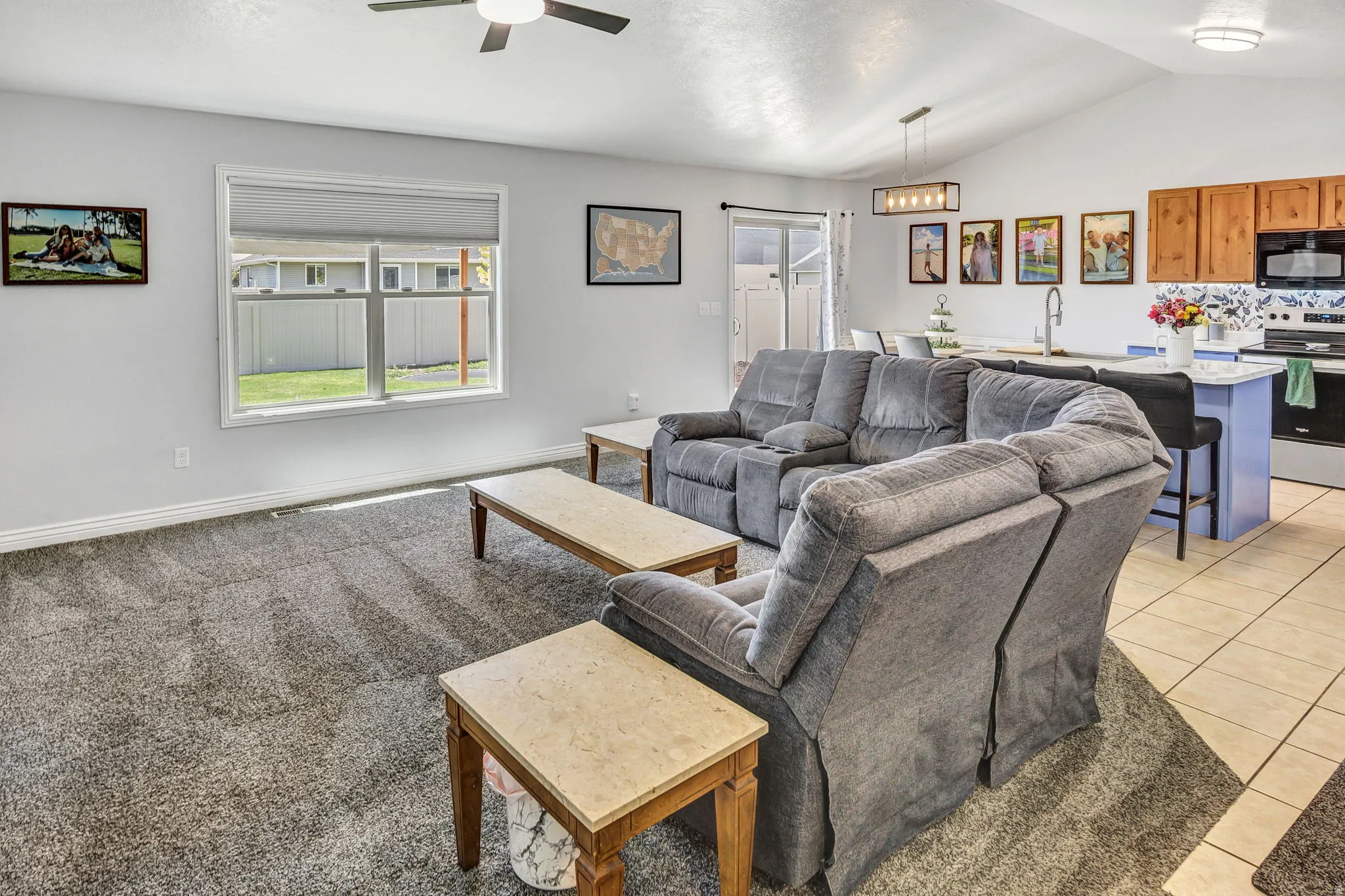 Expansive living area featuring vaulted ceilings with a ceiling fan, a large window offering outdoor views, and durable carpet flooring