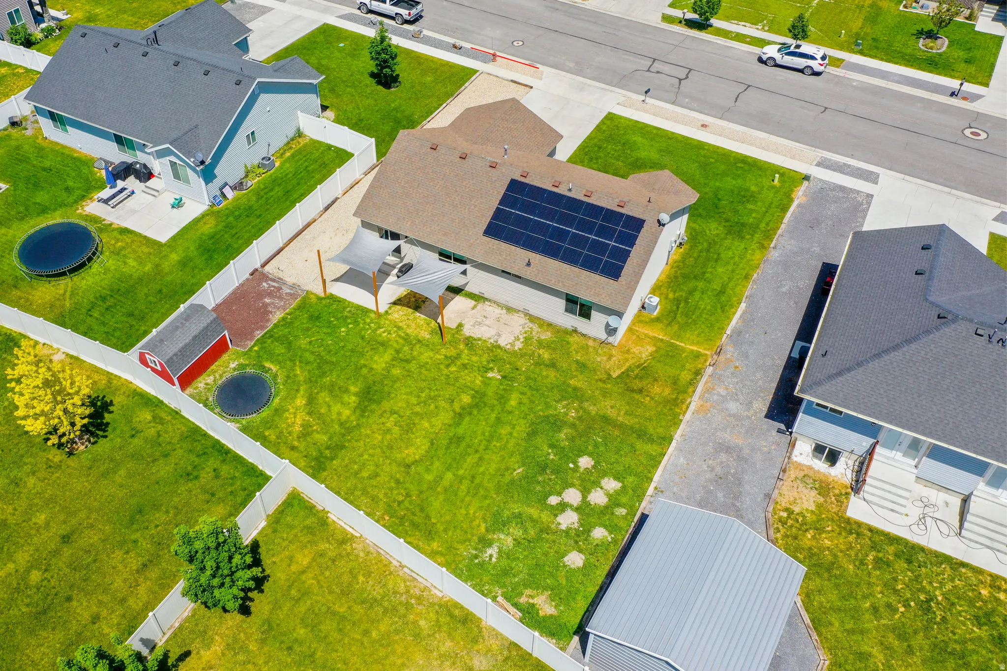 Residential property featuring a brown shingle roof with integrated solar panels, a manicured green lawn, and a light-colored privacy fence