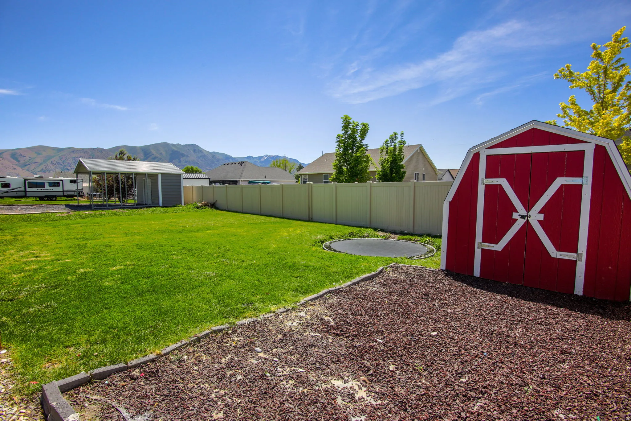 Expansive backyard featuring a red barn-style shed, a separate covered structure, and a perimeter fence