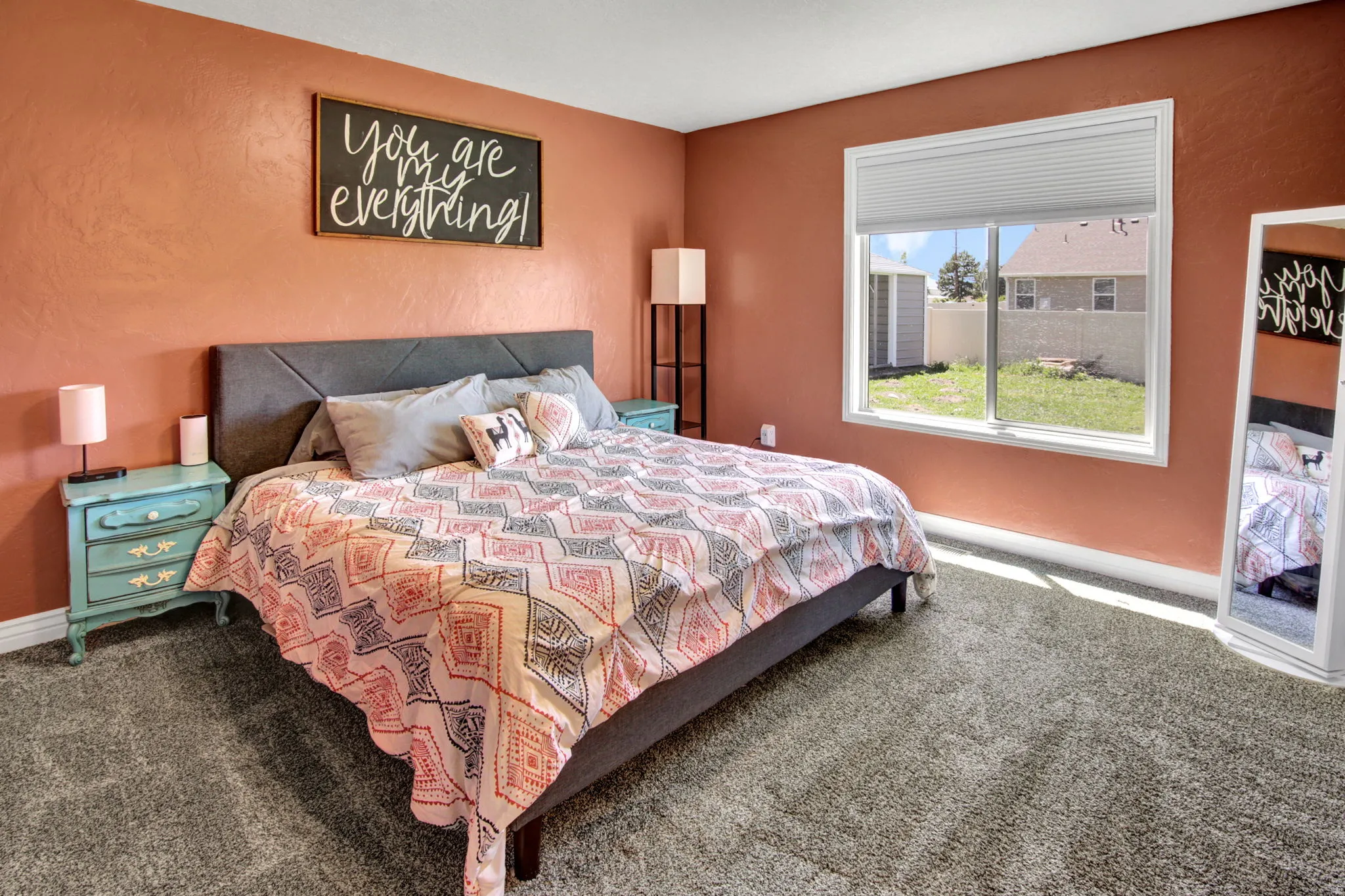 Bedroom featuring textured coral walls, plush gray carpeting, and a large window with privacy blinds