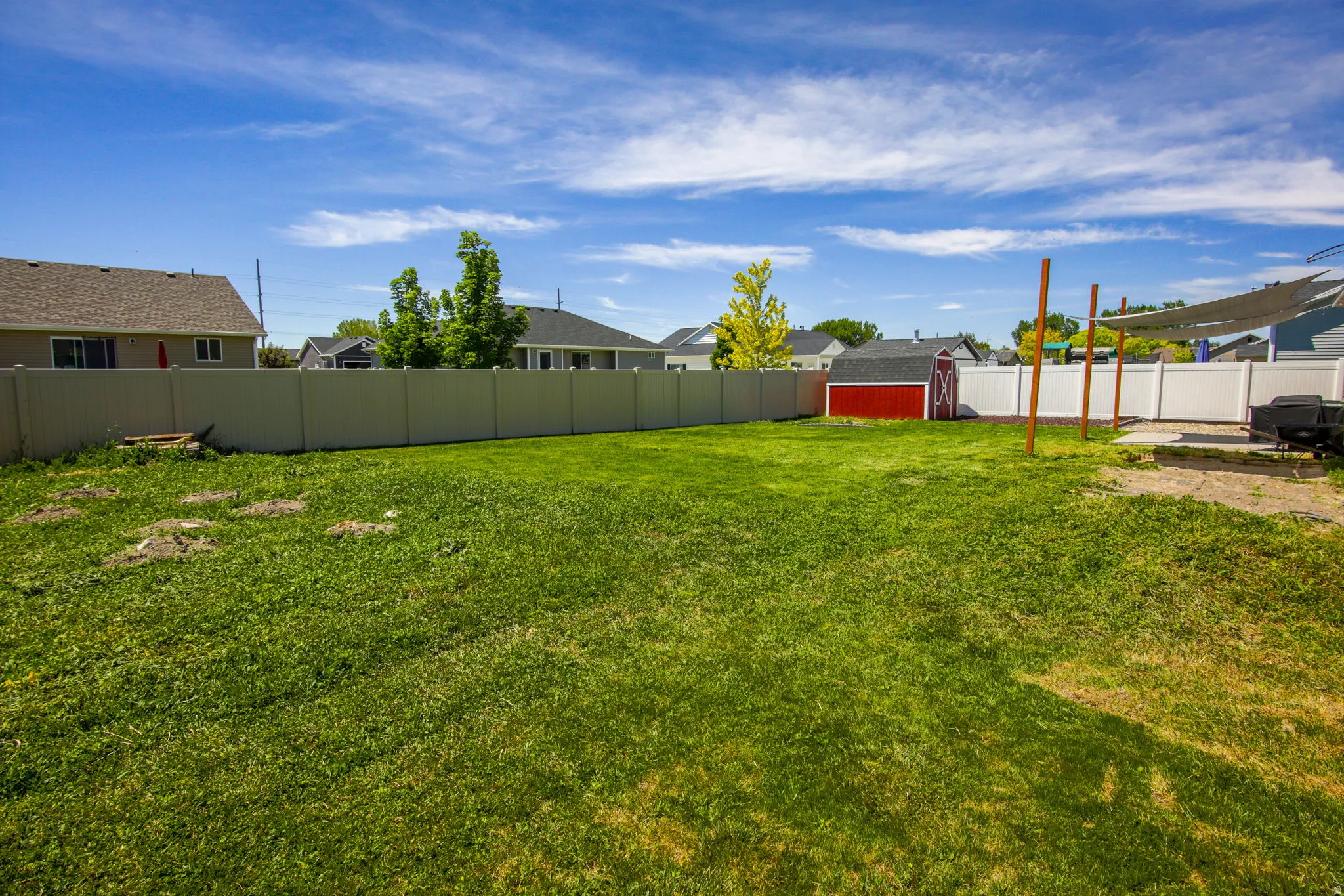 Expansive rear yard featuring a large grass area, a red storage shed, and durable privacy fencing