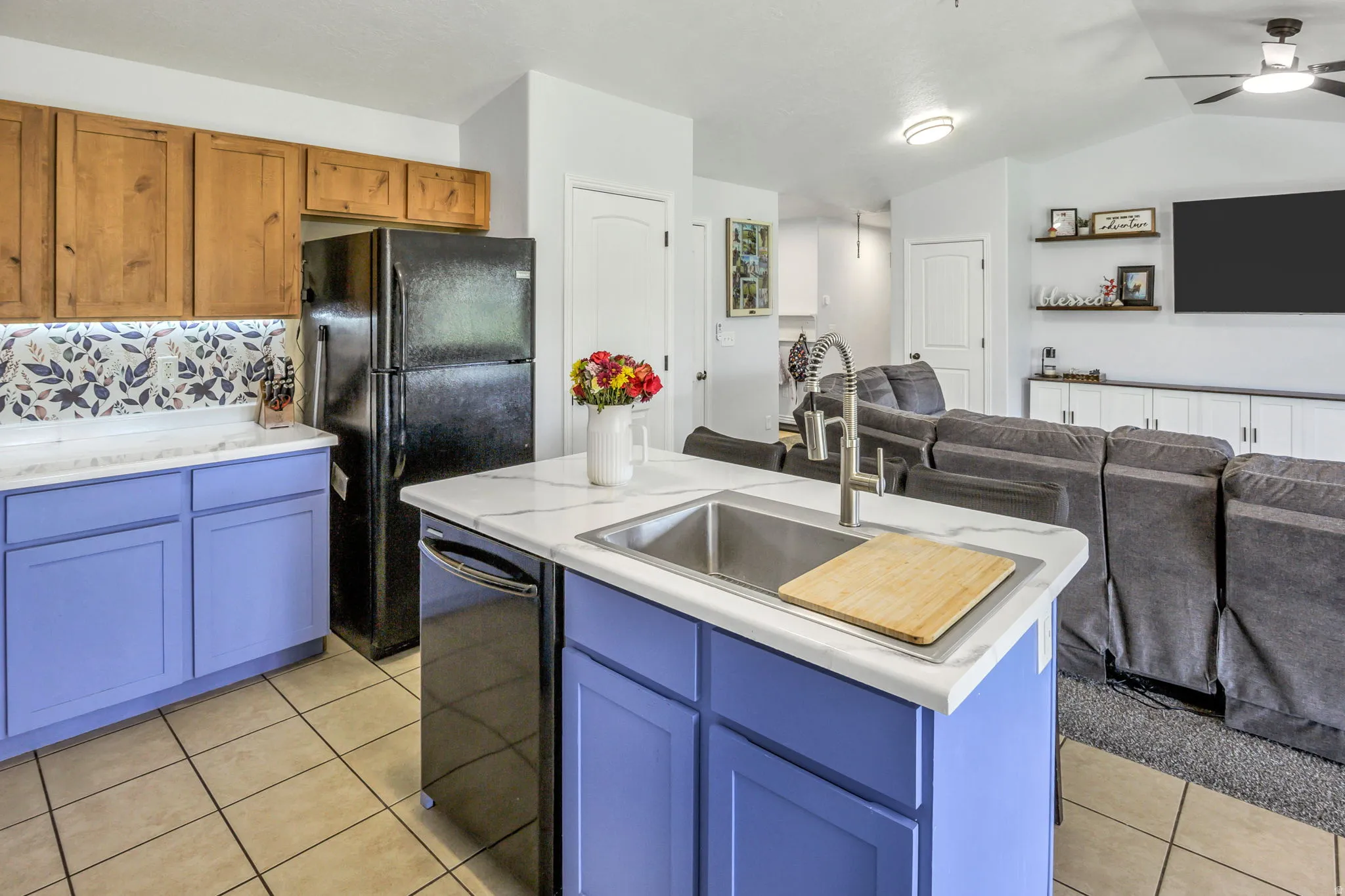 Kitchen featuring custom periwinkle lower cabinetry, natural wood-finish upper cabinetry, a patterned tile backsplash, and an island with an undermount sink