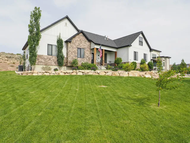 Contemporary farmhouse exterior featuring white board and batten siding, stone accents, black-framed windows, a covered front porch, and a stone retaining wall