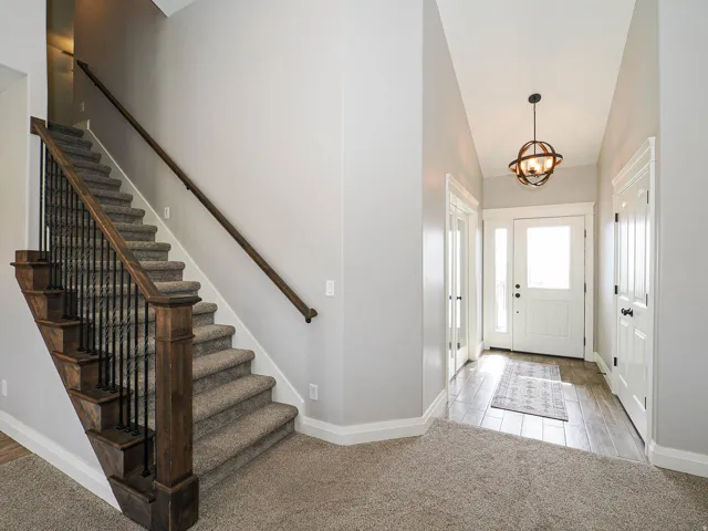 Foyer featuring wood-finish flooring, a white paneled entry door with sidelights, and an open staircase with dark wood newel posts, handrails, and black metal balusters