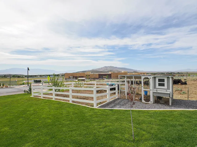 Expansive green lawn featuring a white fence, gravel area, and an animal enclosure
