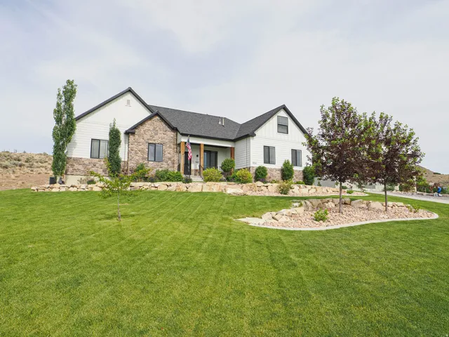 Modern farmhouse exterior featuring white vertical and horizontal siding, natural stone accents, a dark shingle roof, and black-framed windows