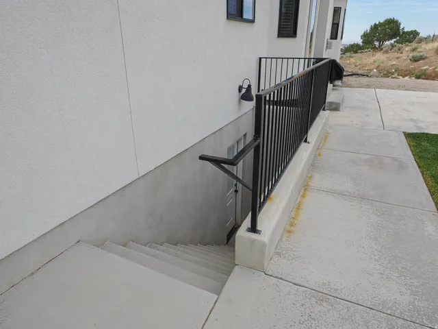Exterior entrance featuring concrete steps, wrought iron handrails, a black wall-mounted light fixture, and a stucco-finish facade