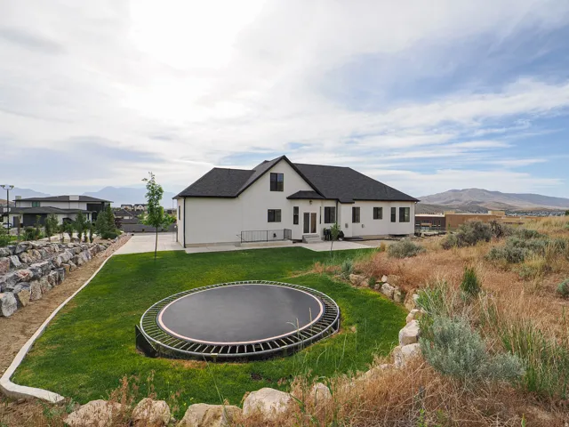 Expansive backyard featuring a manicured lawn, stone retaining walls, and a recessed trampoline