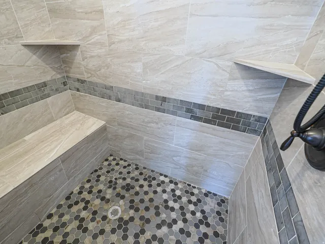 Tiled shower stall featuring a built-in bench, two corner shelves, and a dark bronze shower fixture