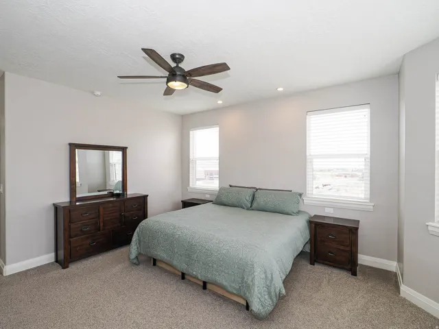 Carpeted bedroom featuring a ceiling fan with integrated lighting, recessed lighting, and two windows with blinds