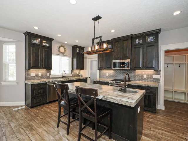 Kitchen featuring dark wood cabinetry, a central island with a sink, stainless steel appliances, a tiled backsplash, and wood-finish flooring
