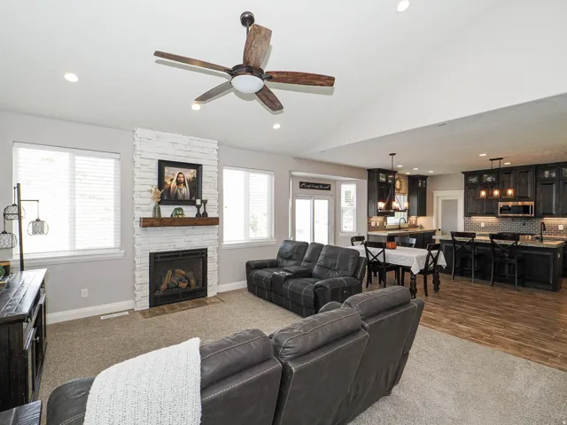 Open concept living space featuring a white stacked stone fireplace with a wood mantel, a vaulted ceiling with a ceiling fan, and recessed lighting