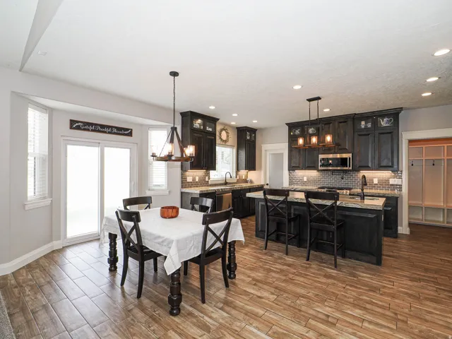 Open-concept kitchen and dining area featuring wood-finish flooring, dark cabinetry, recessed lighting, and a kitchen island with seating