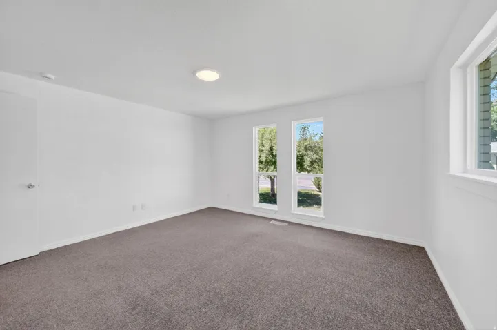 Spacious room featuring white walls, gray carpet, and multiple windows providing natural light