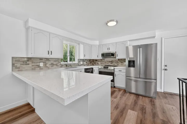 Kitchen featuring white cabinetry, light-toned quartz countertops, a tiled backsplash, stainless steel appliances, and wood-finish flooring