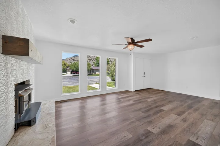 Spacious room featuring a fireplace with a wood mantle, wood-finish flooring, a ceiling fan, and multiple windows