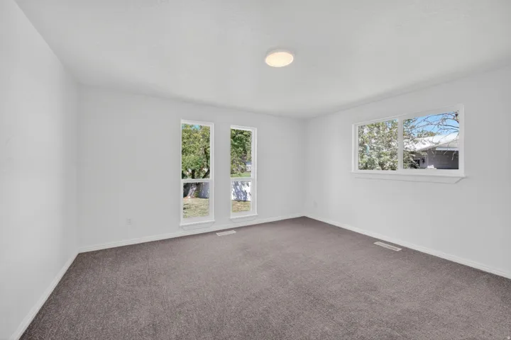 Spacious room featuring white walls, gray carpet, multiple large windows, and a flush-mount ceiling light