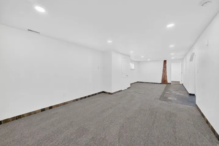 Spacious room featuring recessed lighting, a combination of gray carpeting and dark slate-style tile flooring, and a decorative wooden column