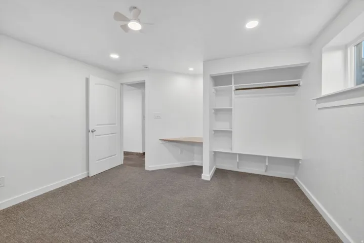 Carpeted room featuring a built-in closet system with shelving and hanging rod, a built-in desk, a ceiling fan, and recessed lighting