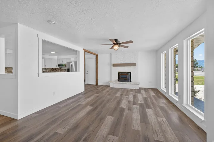 Spacious living area featuring wood-finish flooring, a white brick fireplace with a wood mantle, and a ceiling fan