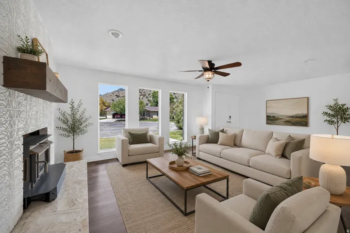 Bright living space featuring a tiled fireplace with a wood mantle, wood-finish flooring, a ceiling fan, and multiple large windows