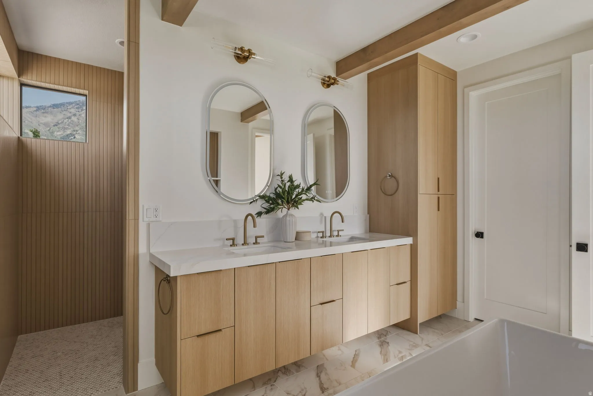 Double vanity with light wood cabinetry, white stone countertop, dual undermount sinks, and brass-finish fixtures