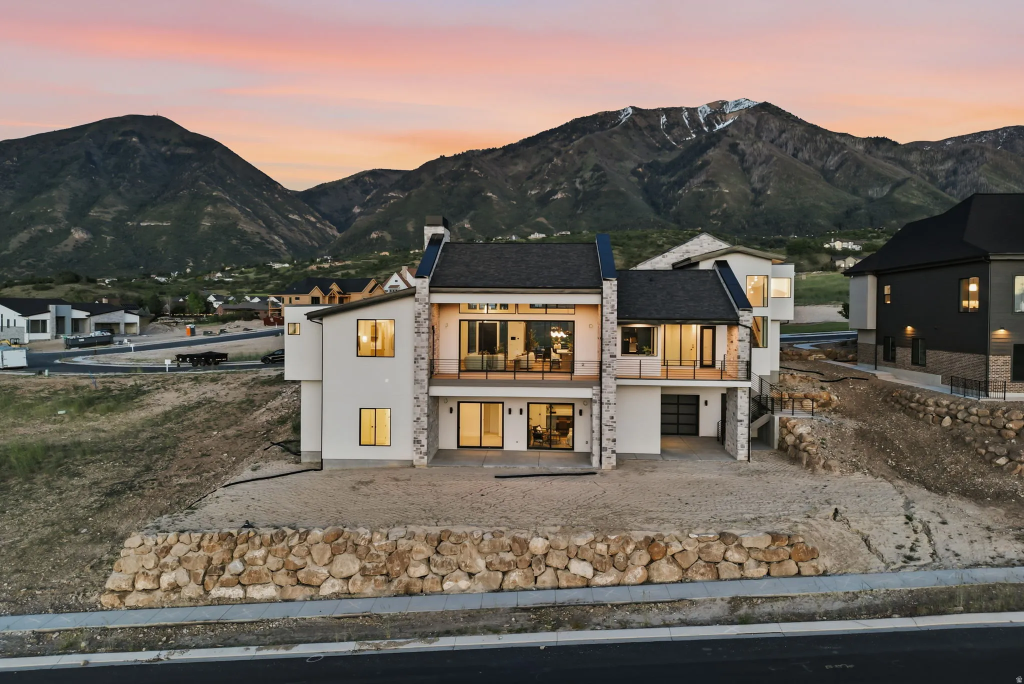 Contemporary architecture featuring a multi-story design with extensive rear balconies, stone facade accents, a dark shingled roof, and a prominent mountain backdrop