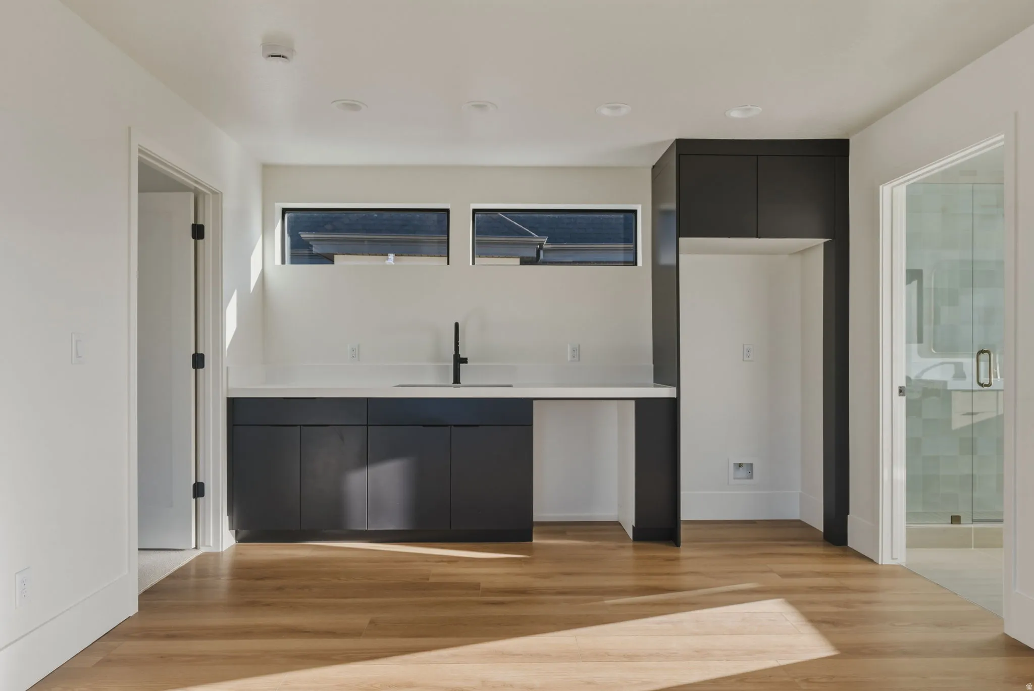 Modern kitchenette featuring dark cabinetry, white countertops, a sink with a matte black faucet, and a built-in appliance alcove