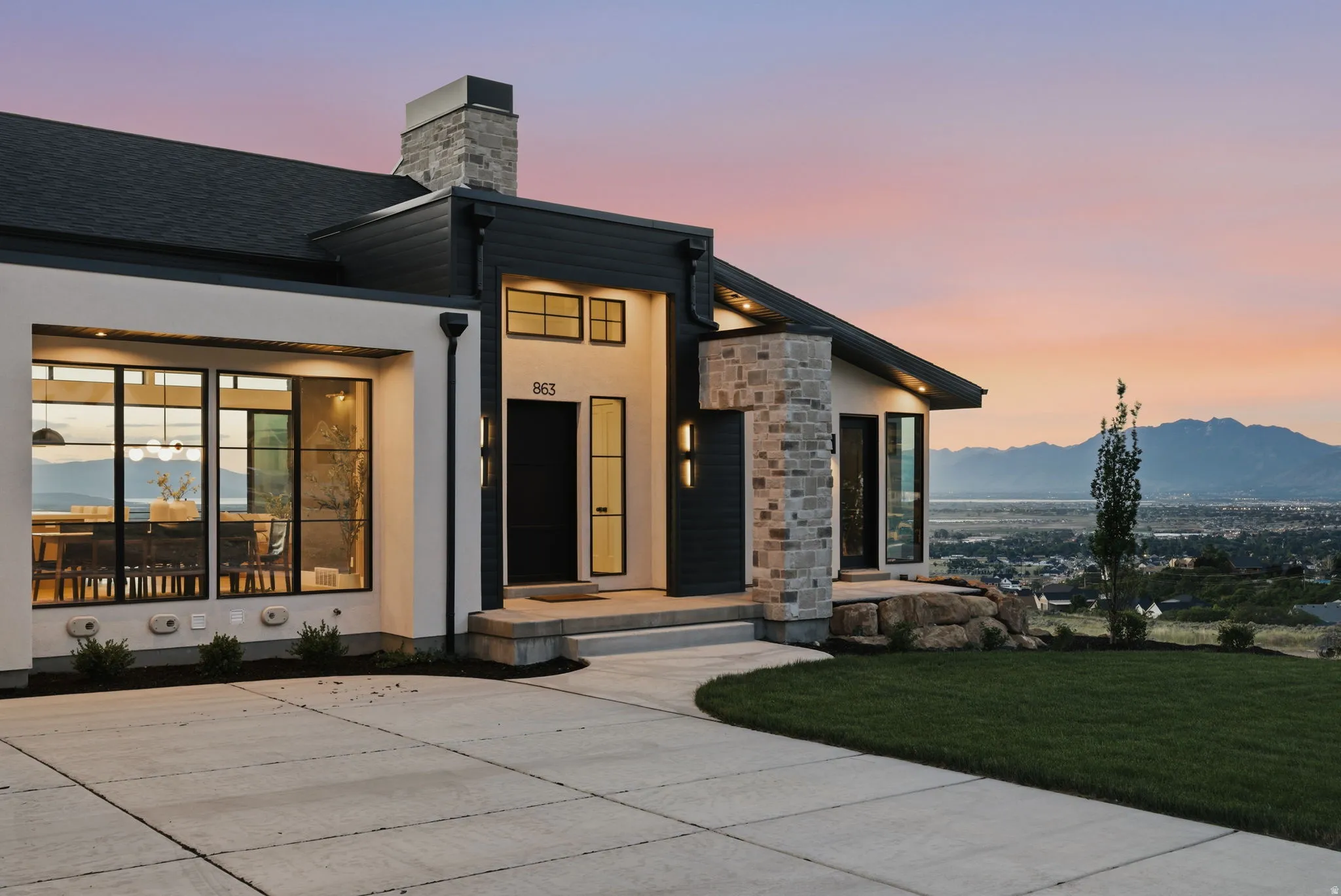 Contemporary exterior featuring a stone chimney and column, dark siding, and large window installations