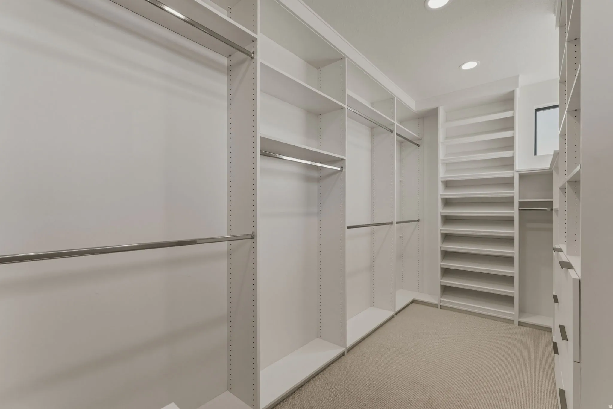 Custom closet system featuring multiple hanging rods, extensive shelving, built-in drawers, recessed lighting, and a window