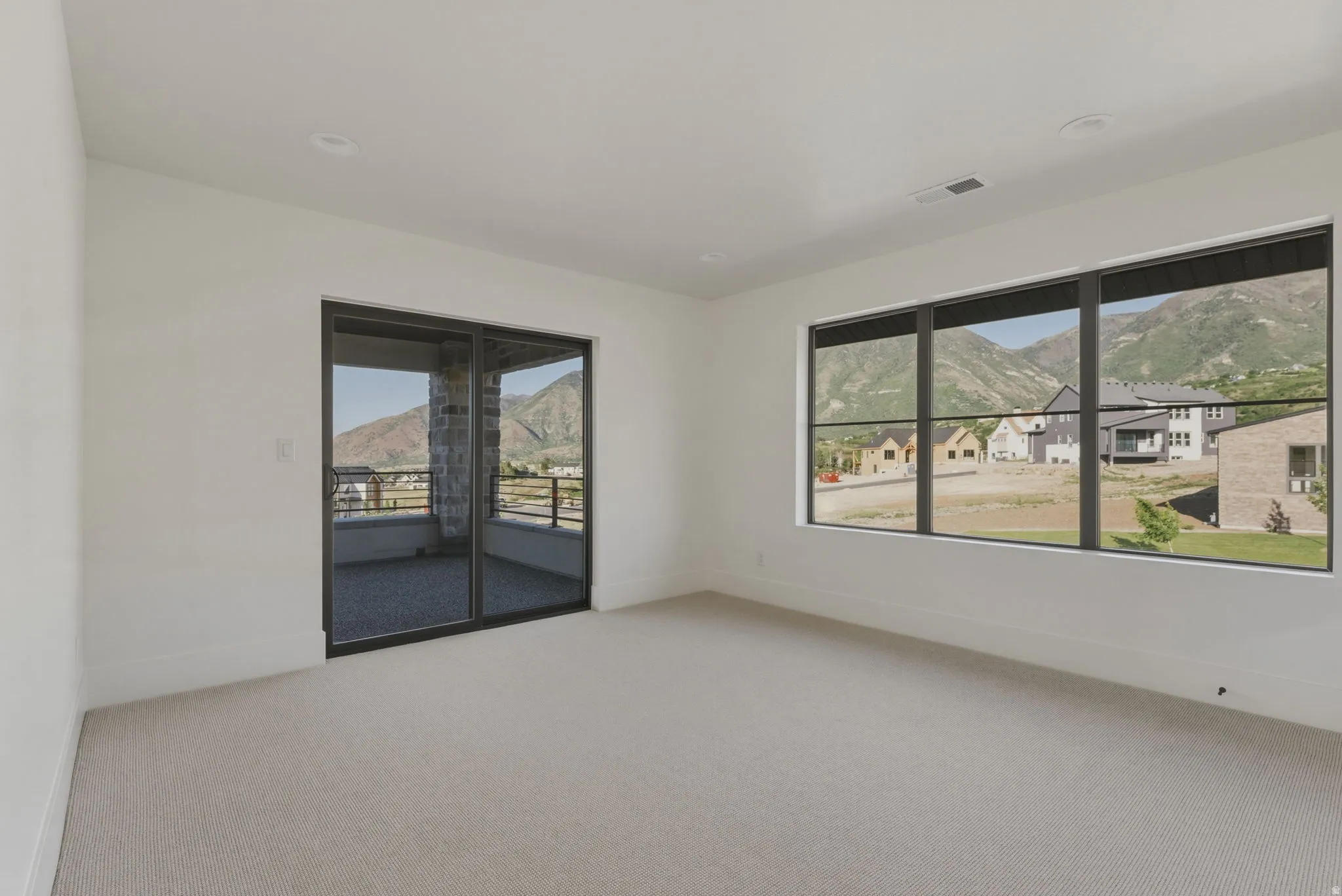 Light-toned carpeted room featuring a full-width window with black frames, offering expansive mountain scenery