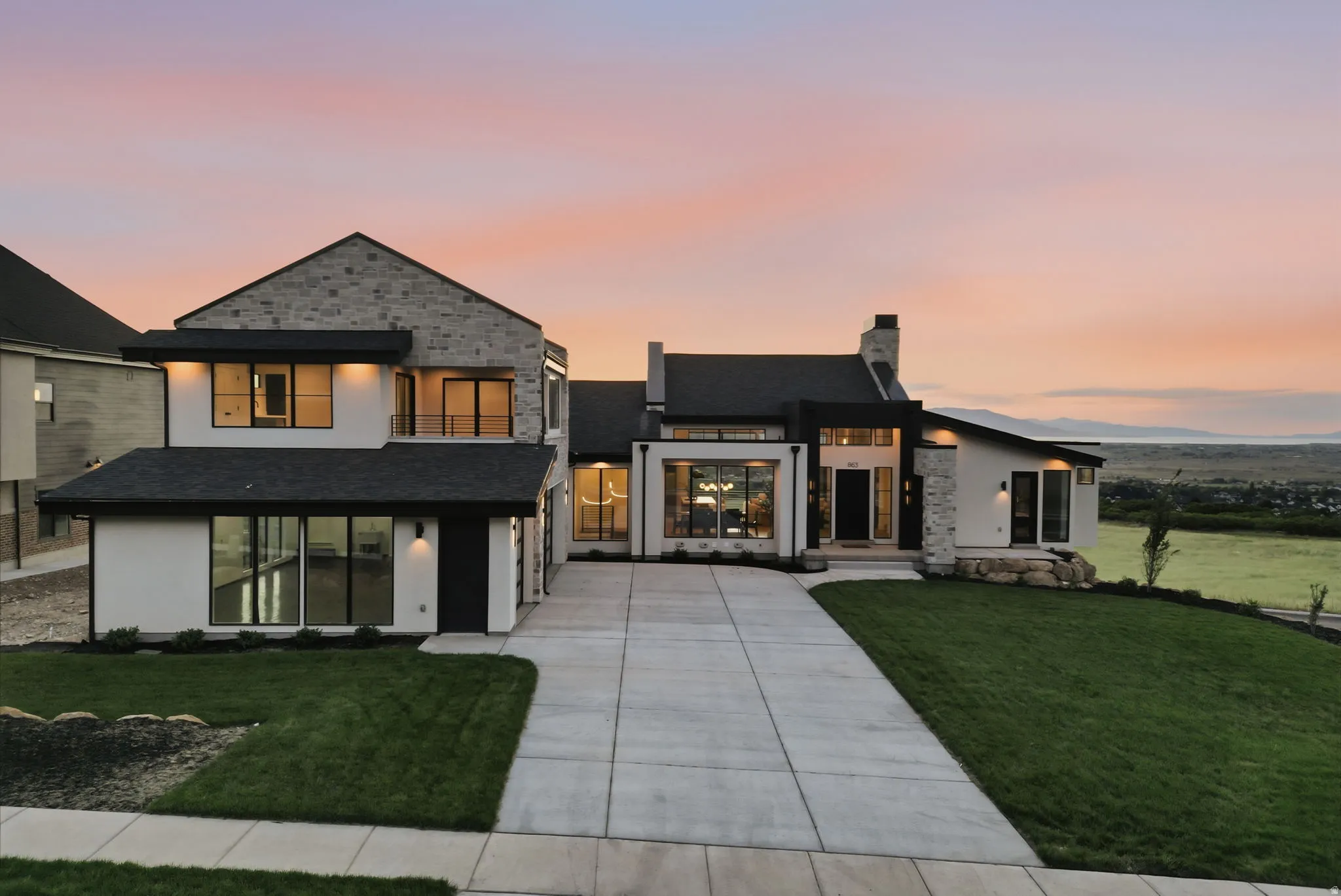 Contemporary exterior featuring a stone and stucco facade, dark trim accents, expansive windows, a concrete driveway, and a manicured lawn
