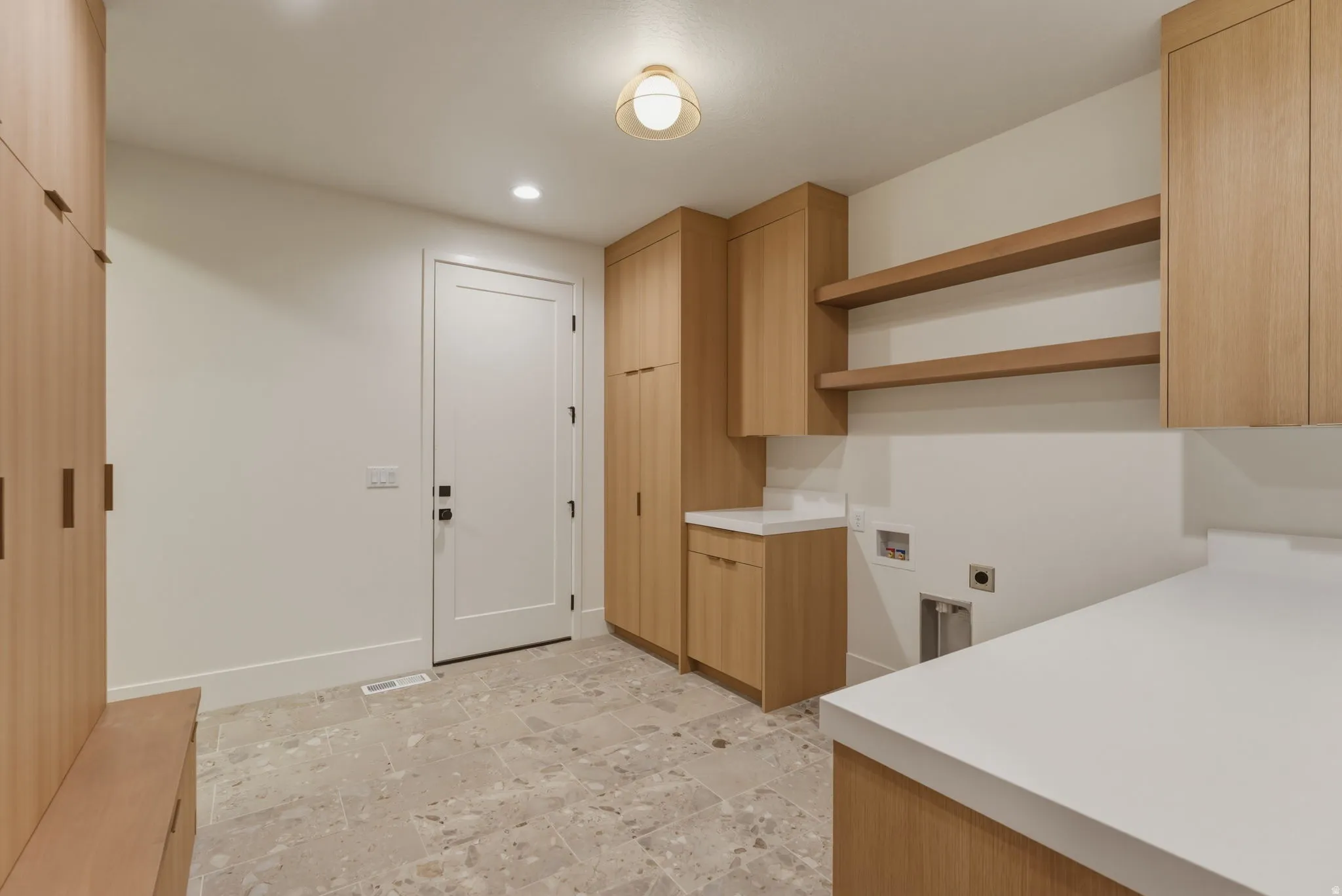 Laundry/Mud Room featuring light wood-finish cabinetry, white solid surface countertops, and light-toned stone-finish tile flooring