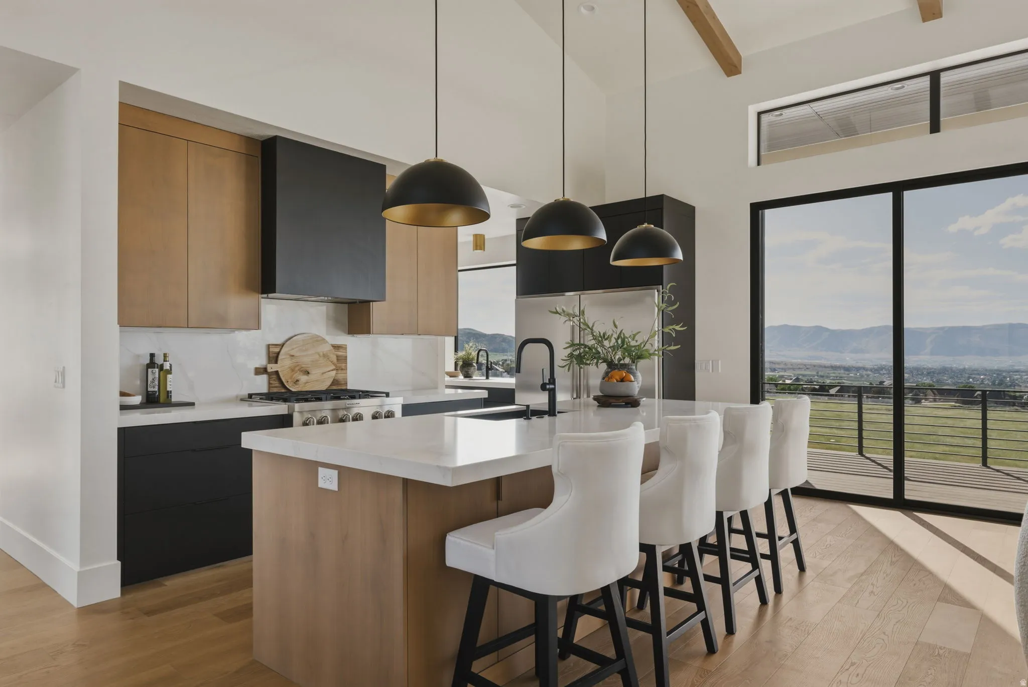 Open-concept kitchen featuring an oversized island with white countertop, black and wood-finish cabinetry, a gas range with a black range hood, and wood-finish flooring