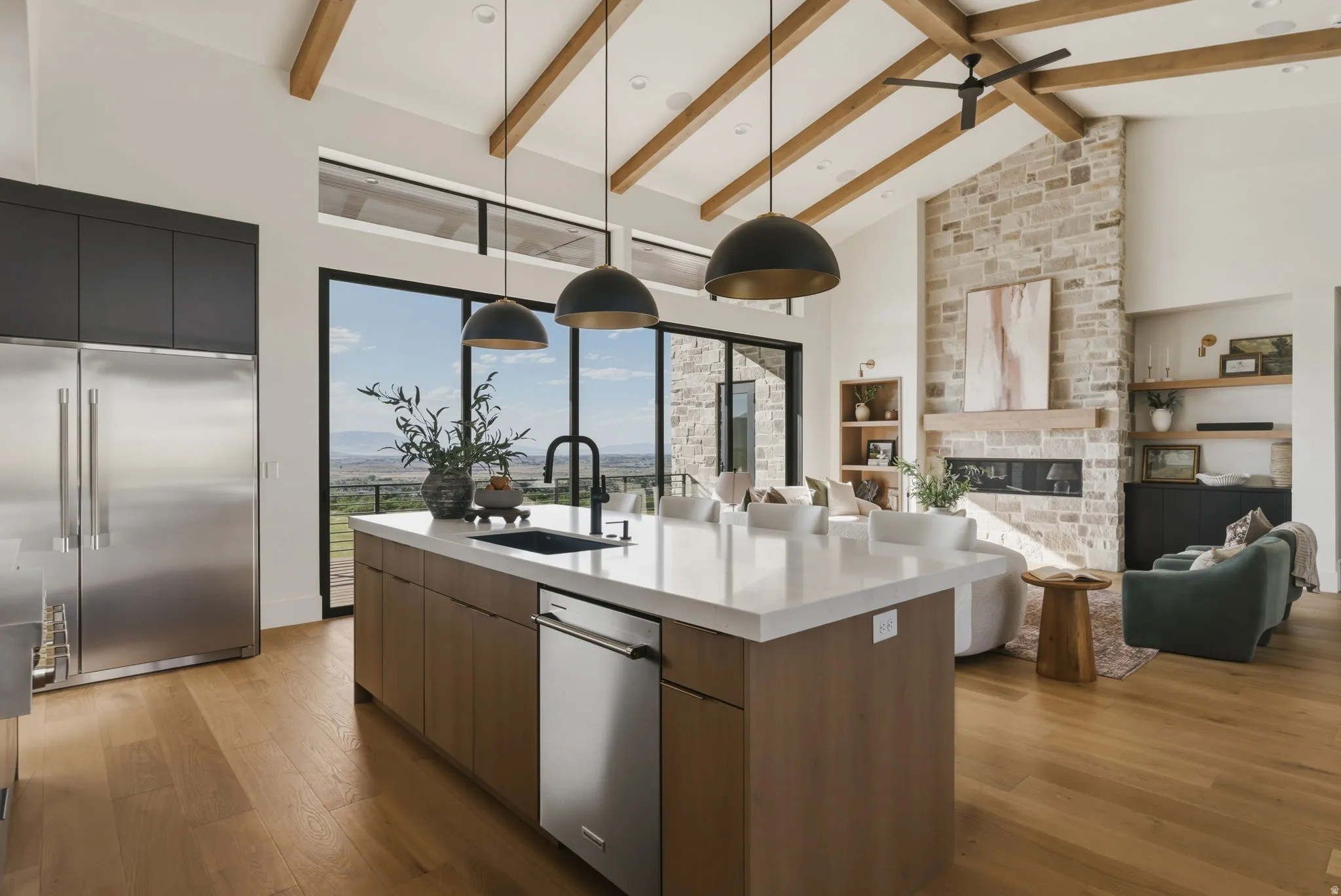 Open-concept living space featuring a spacious kitchen island with a white countertop and undermount sink, stainless steel appliances, and wood-finish flooring