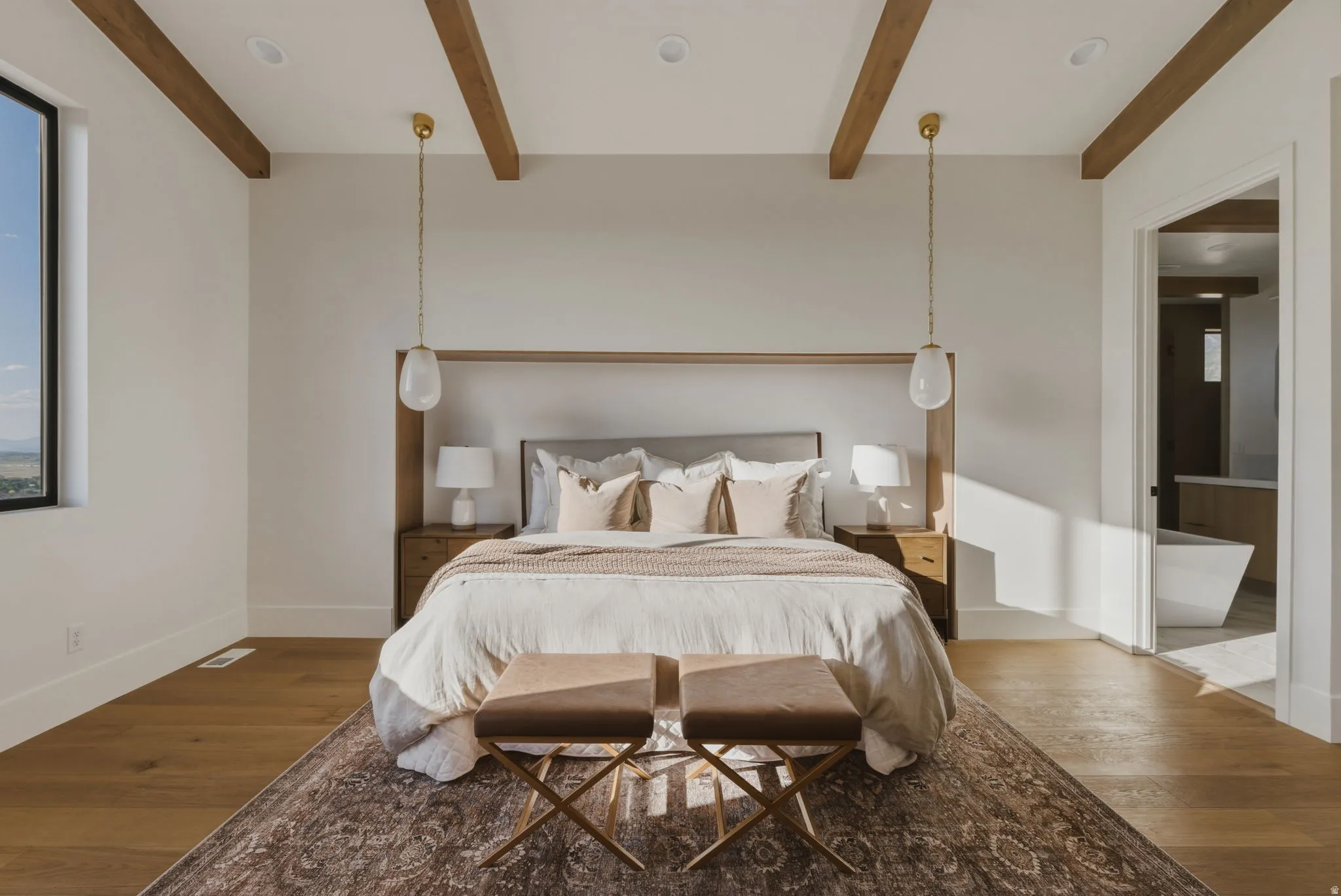Bedroom featuring exposed wood ceiling beams, a large window, wood-finish flooring, recessed lighting, and an open doorway to an adjoining bathroom with a freestanding tub