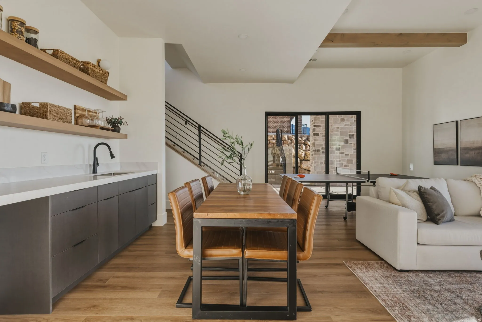 Open-concept living area featuring wood-finish flooring, a contemporary wet bar with floating shelves, and a modern staircase with metal railings