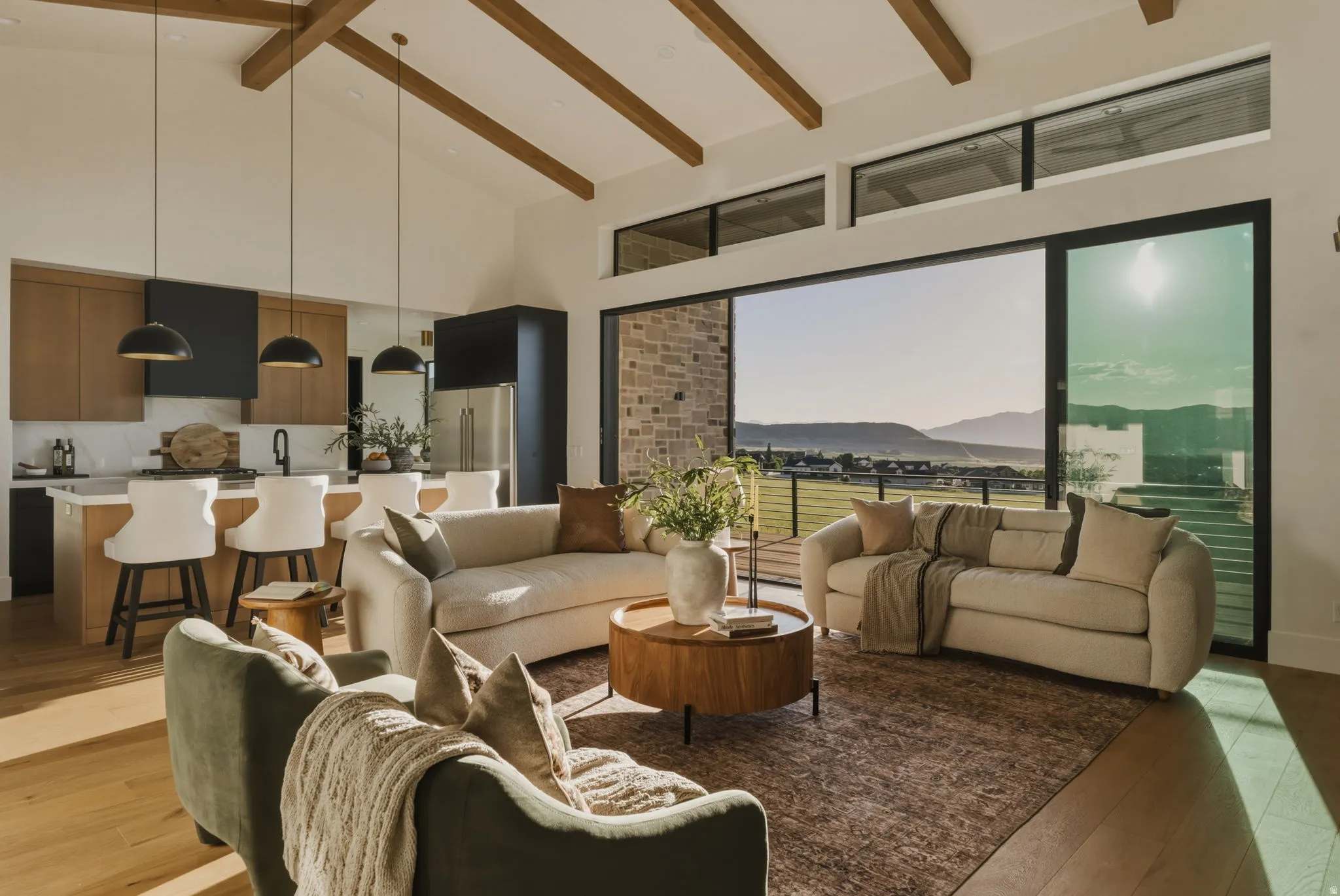 Spacious open-concept living area featuring exposed wood beams, wood-finish flooring, and a stone accent wall