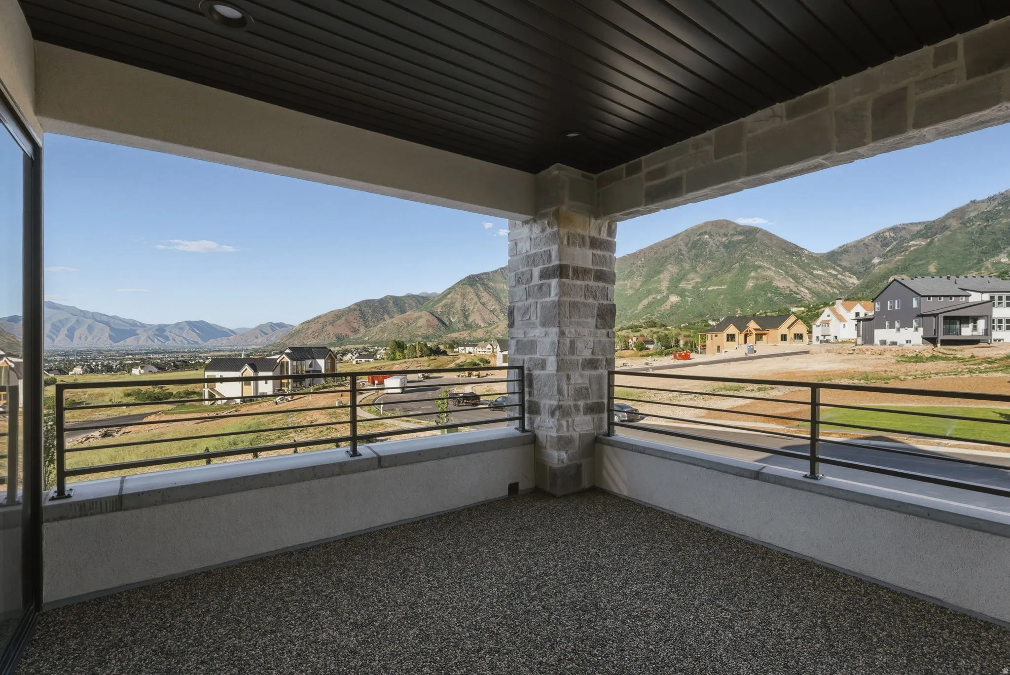 Covered outdoor patio featuring exposed aggregate flooring, stone pillars, and dark metal railings