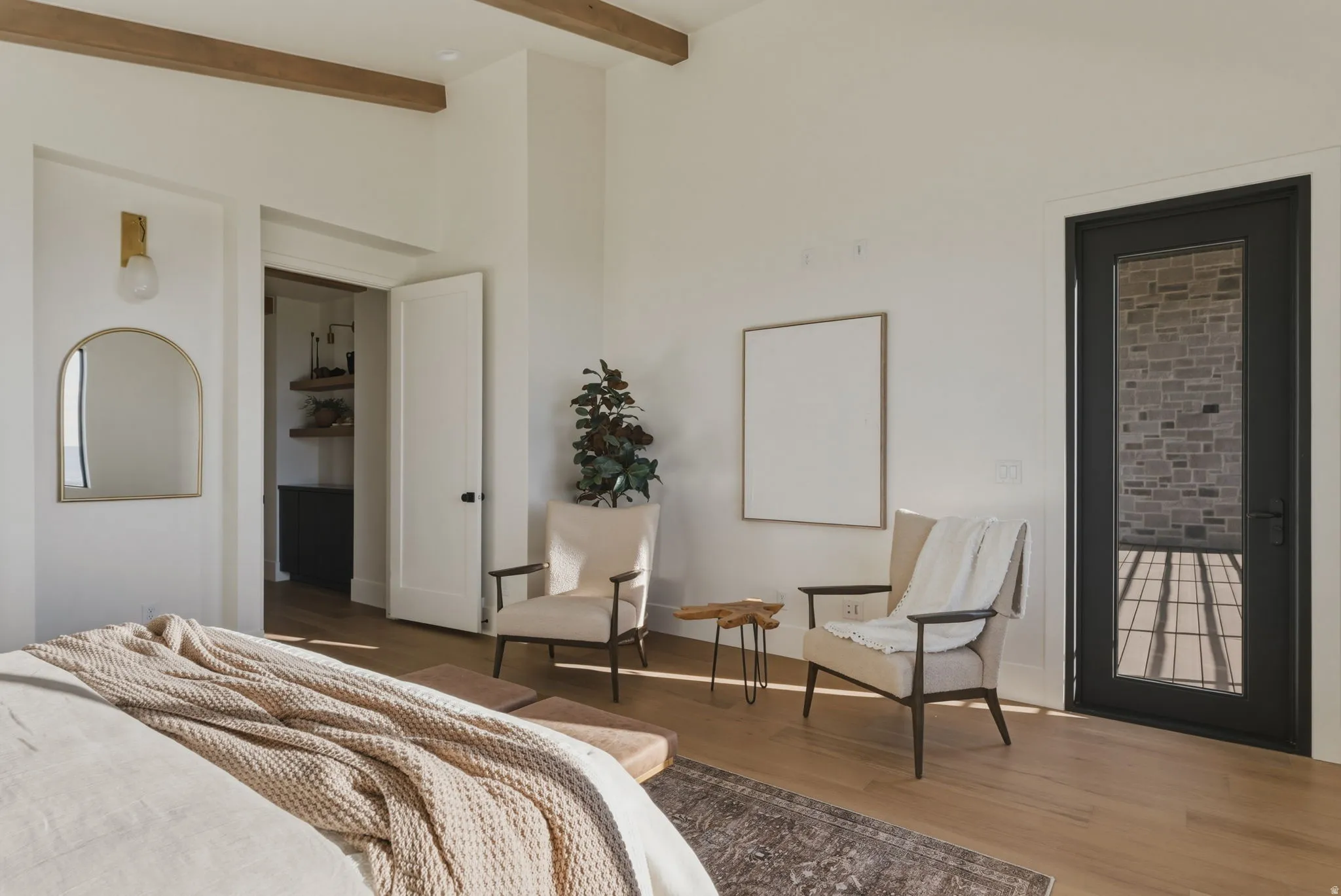 Spacious interior featuring exposed ceiling beams, wood-finish flooring, a wall-mounted sconce, and a full-light exterior door with a dark frame
