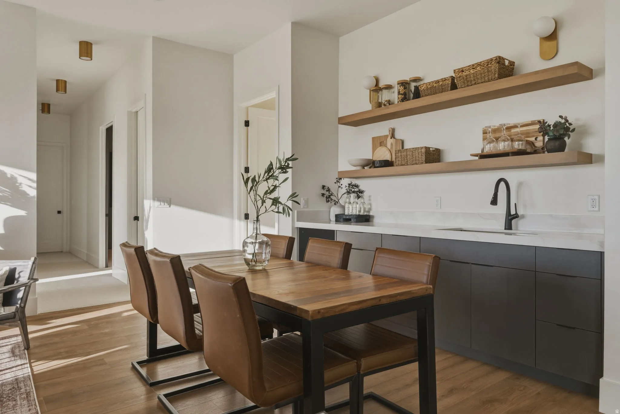 Dining area featuring wood-finish flooring, a built-in wet bar with a single basin sink, matte black faucet, light-toned countertop, and open shelving