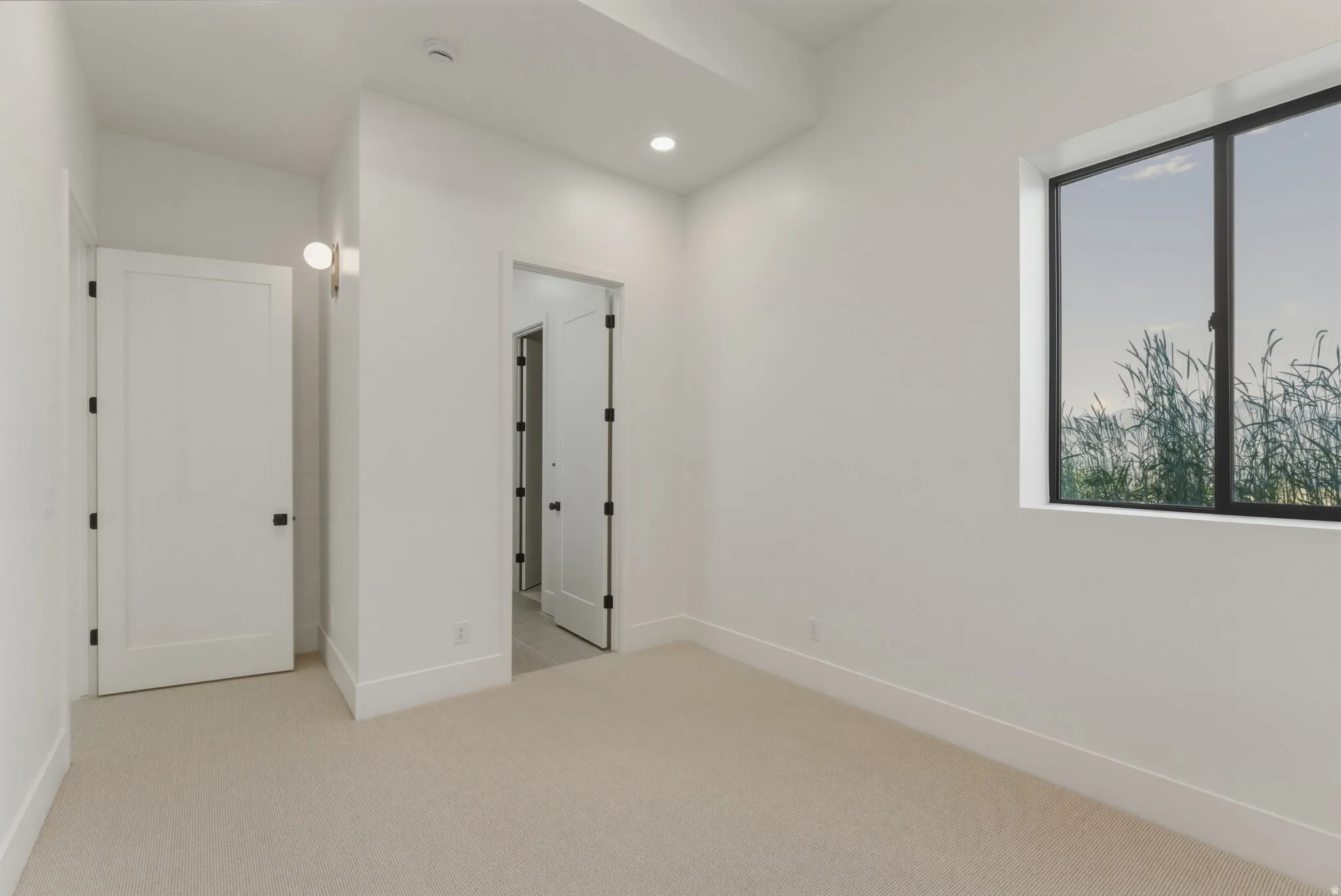 Neutral toned carpeted room featuring white walls, recessed lighting, and a square window with dark framing