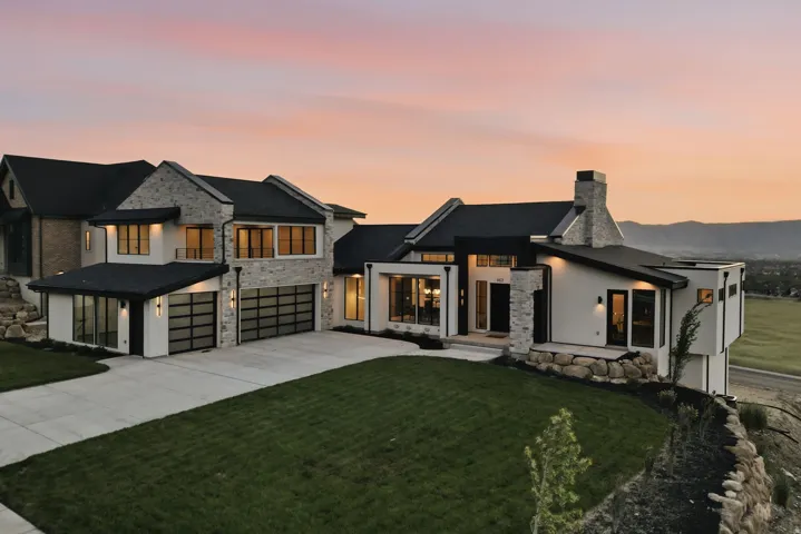 Modern architectural residence showcasing a stone and stucco exterior, multiple large windows with black frames, a prominent stone chimney, and a multi-car garage with frosted glass doors