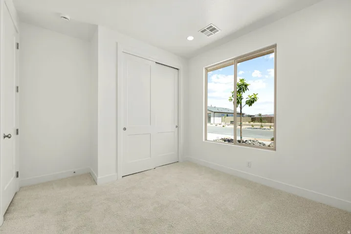 Bedroom with neutral carpeting, white walls, a large window, and a double sliding closet door