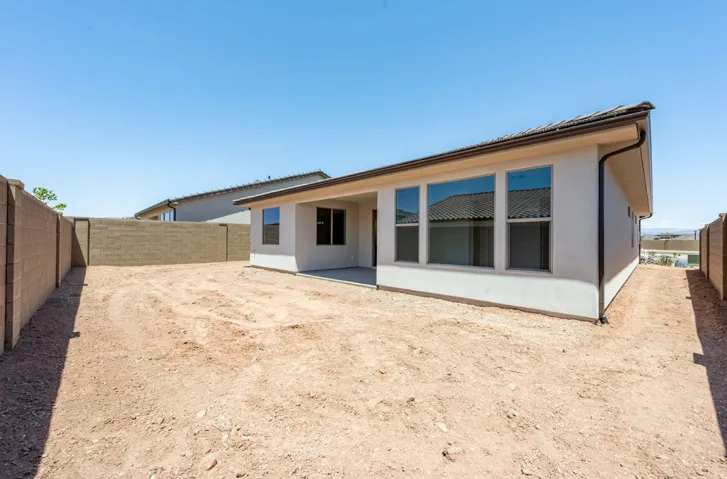 Private backyard featuring a stucco exterior with a covered patio, multiple windows, and block wall fencing