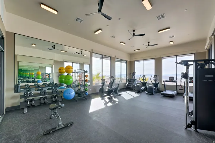 Spacious fitness center featuring expansive windows, recessed lighting, ceiling fans, full-height wall mirrors, and rubberized flooring