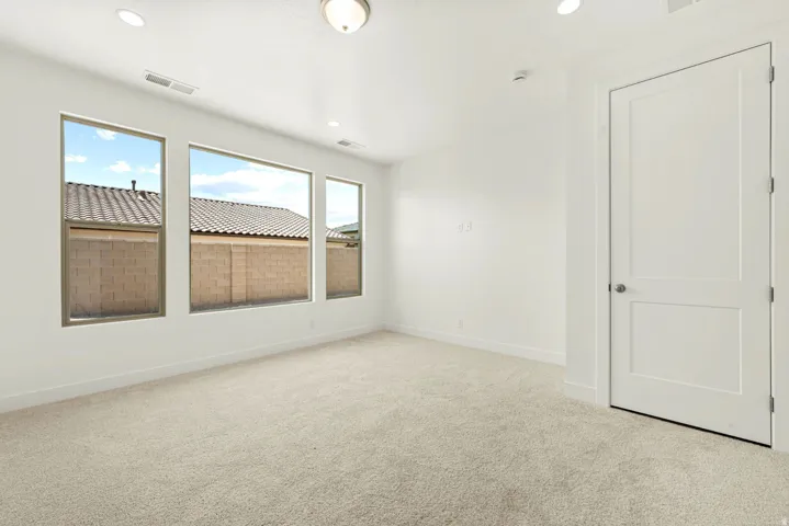 Spacious room featuring three large windows, recessed ceiling lighting, a paneled interior door with a brushed nickel knob, and light-toned carpet flooring