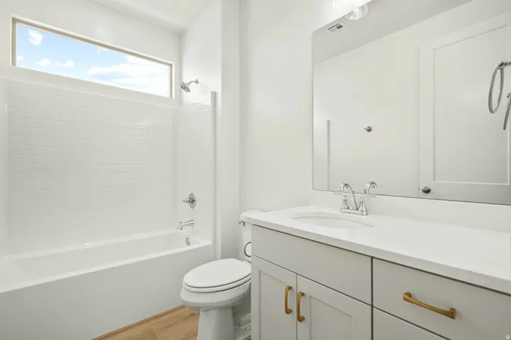 Bathroom featuring a white subway tile tub surround, transom window, wood-finish flooring, a vanity with a white countertop, and a vanity mirror